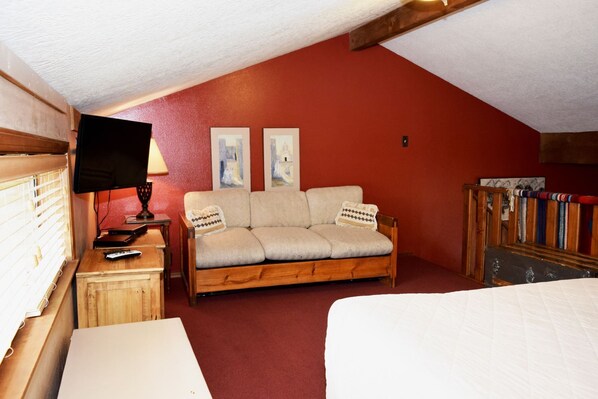 A cozy room with a wooden sofa, a television, and two framed pictures on the wall.
