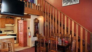 Un espace repas avec un escalier en bois, une cuisine dotée de meubles en bois et un téléviseur à écran plat fixé au-dessus du comptoir.