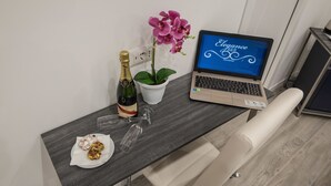 Una computadora portátil sobre un escritorio con una botella de champán, una copa y un plato de comida.