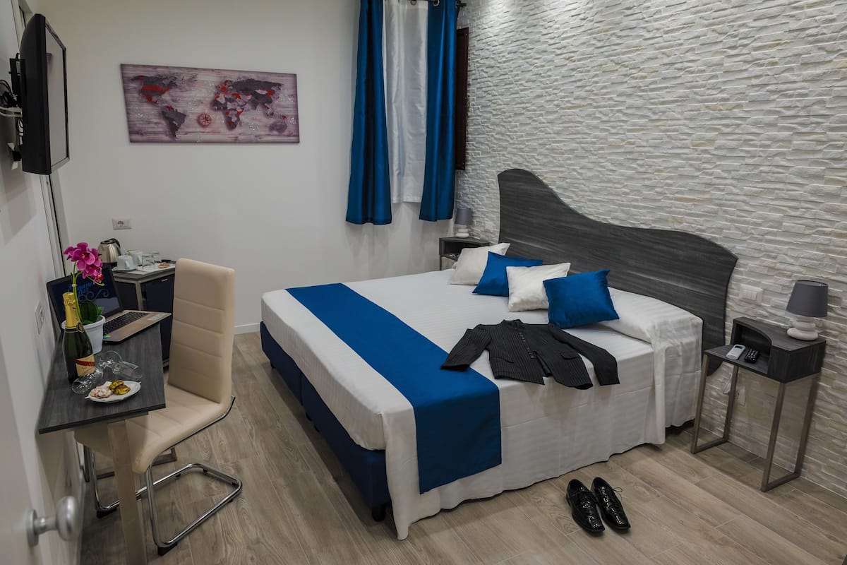 Een moderne hotelkamer met een bed, een bureau, een stoel, een klein tafeltje met een fles en glazen, en een wereldkaart aan de muur.