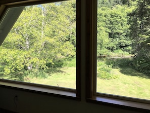 Enjoy a serene view of the surrounding landscape from this room's window, overlooking a grassy area with trees and a body of water.