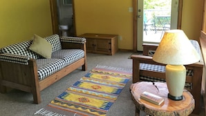 Uma sala de estar aconchegante com um sofá xadrez, uma mesa de centro de madeira, um tapete colorido, um abajur e uma obra de arte em formato de coração na parede.