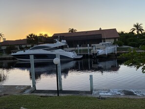 Enjoy serene waterfront views from the marina, where two yachts are docked amidst lush greenery and palm trees.