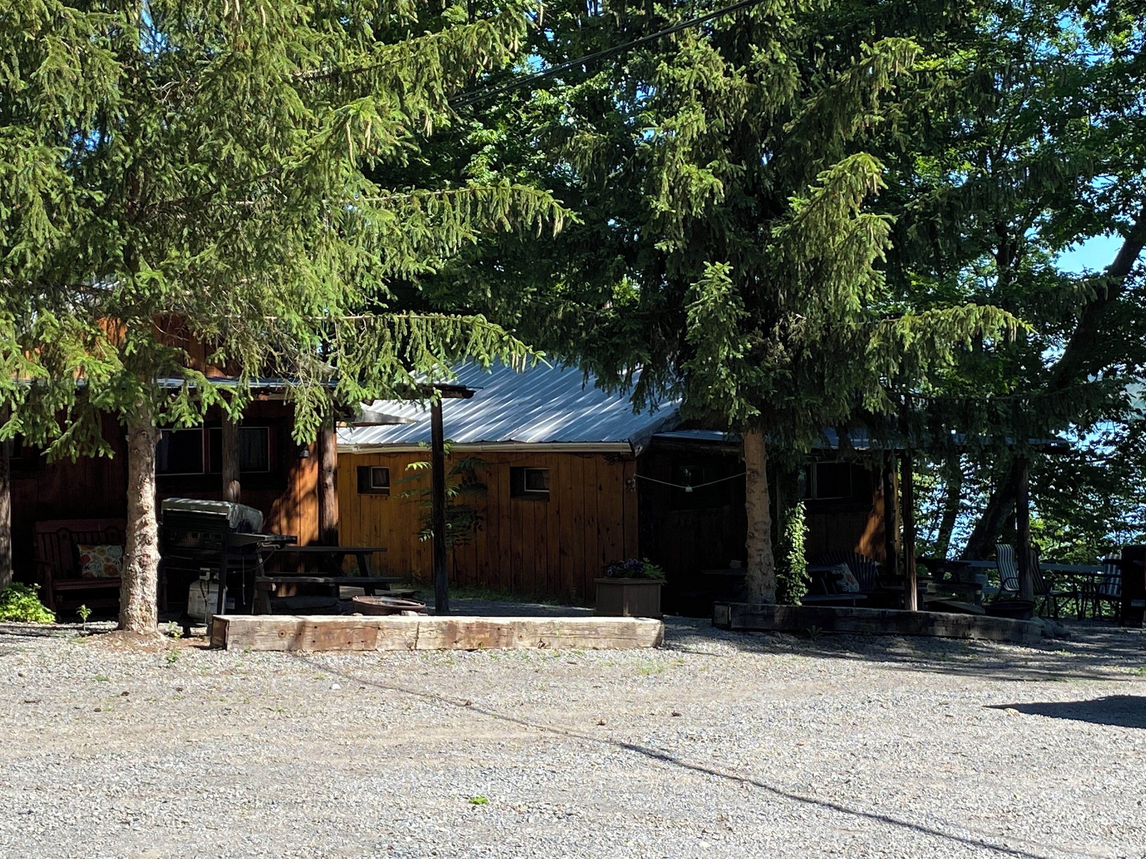 Uma cabana rústica com acesso por um caminho de cascalho, rodeada por árvores.