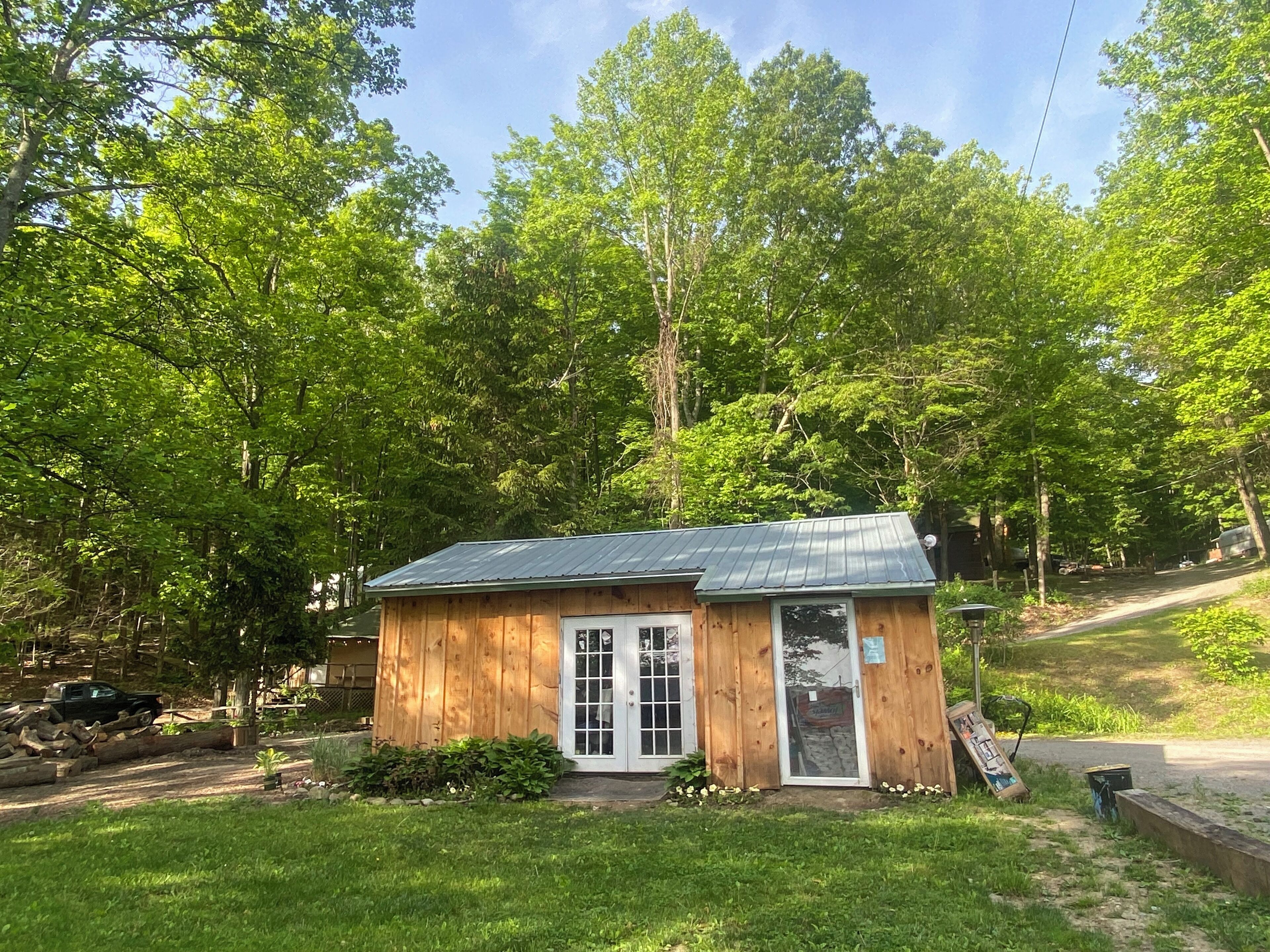 A small wooden cabin with a metal roof, surrounded by lush green trees.