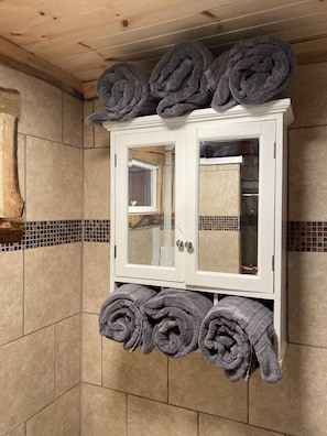 Un baño con un mueble blanco que contiene toallas enrolladas y un espejo.