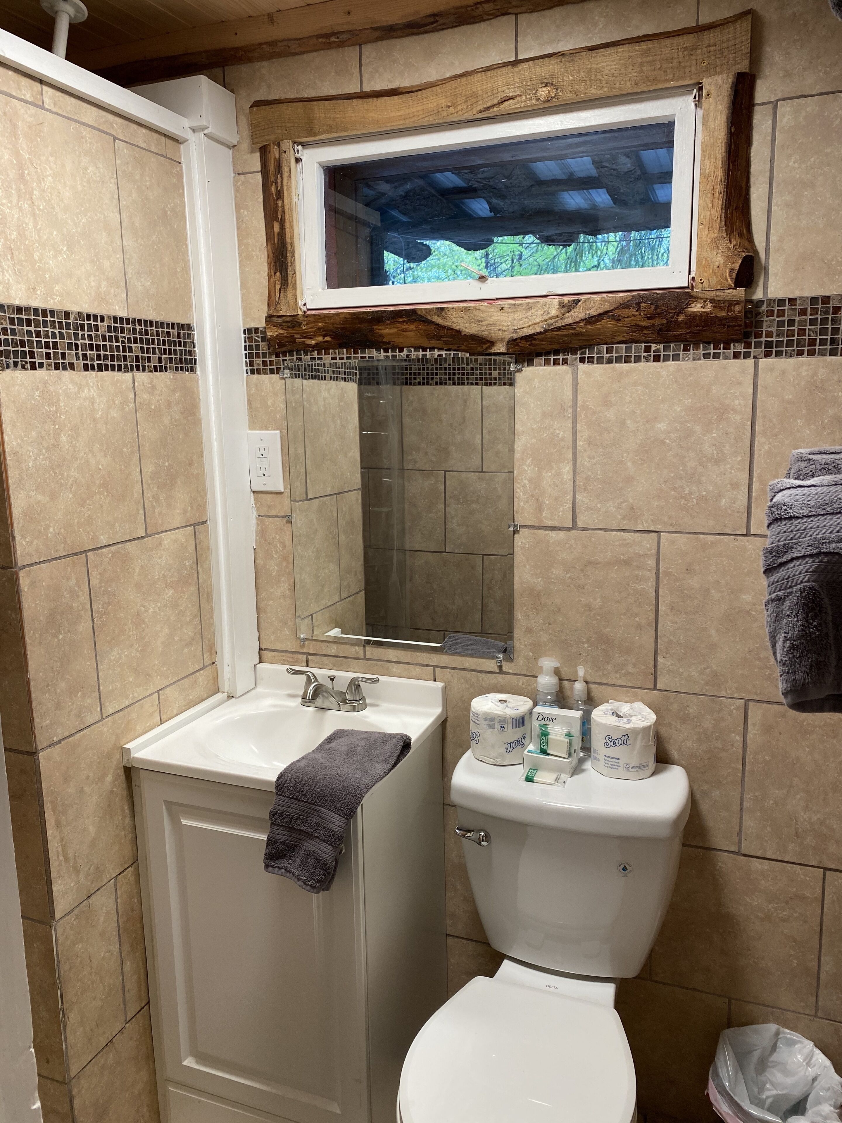 A bathroom with a shower, sink, toilet, and a window above the toilet.