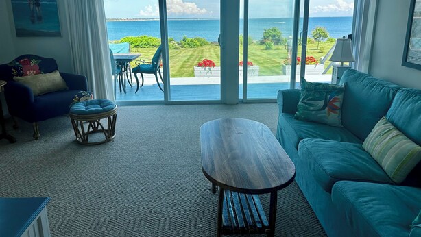 A spacious living room with a large sliding glass door leading to a balcony with a view of the ocean.