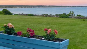 A grassy area with a wooden bench and flower beds, overlooking a body of water and a distant shoreline.
