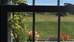 A view through a window with a view of the sea and a grassy area with flowers.