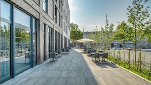 A modern outdoor seating area with tables and chairs, large windows, and a view of the street. - Four Points Flex by Sheraton Bochum (Bochum)