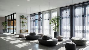 A modern interior with large windows, grey sofas, and potted plants. - Four Points Flex by Sheraton Bochum (Bochum)