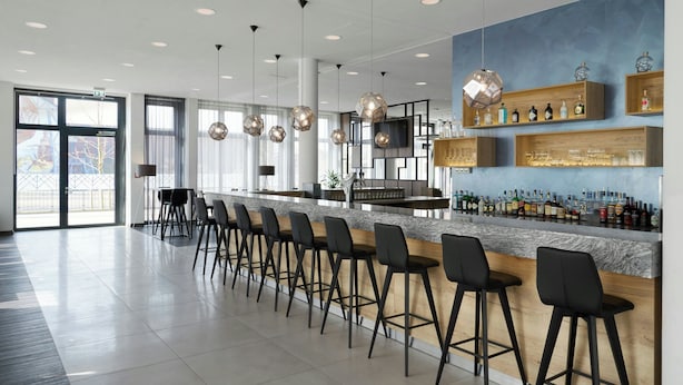 A modern bar area with a long counter, black bar stools, and shelves with bottles. - Four Points Flex by Sheraton Bochum (Bochum)