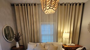 A neatly made bed with a large, ornate chandelier above it, a bedside table with a lamp, and a window with sheer curtains. - Adorable Intown Duplex Close to Downtown Atlanta; 5 minute walk to Beltline (Atlanta)