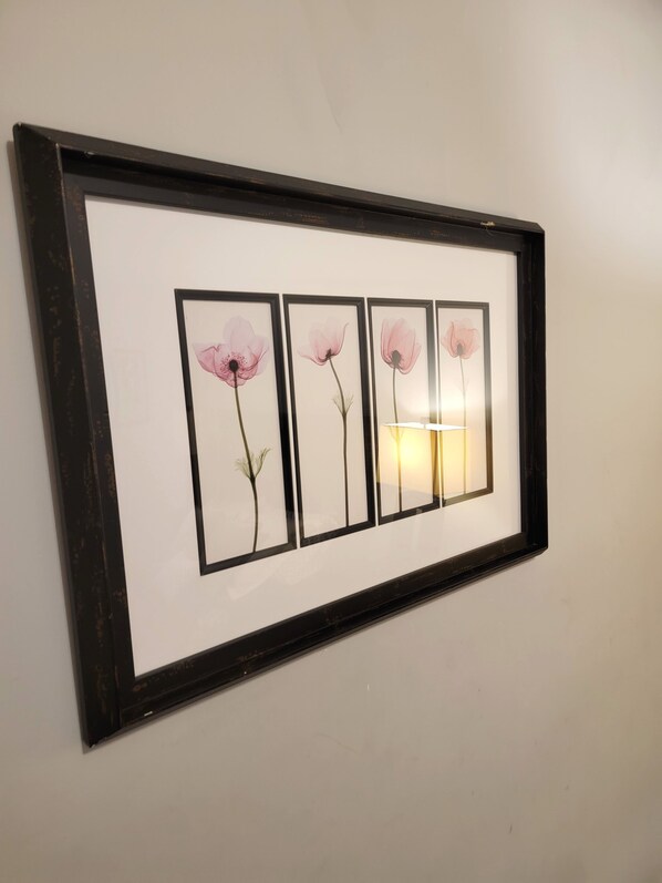 A framed artwork of four pink flowers on a wall.
