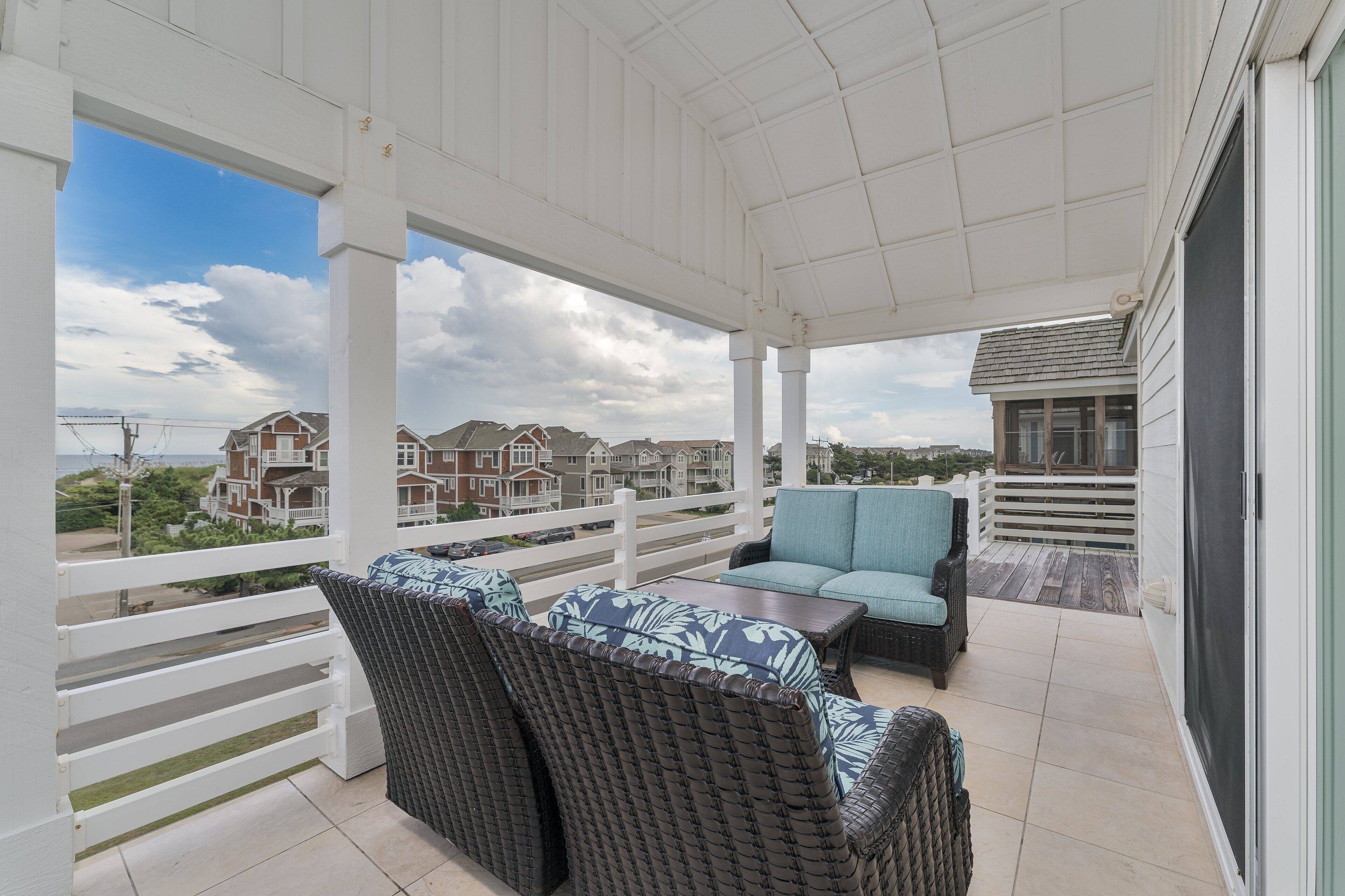 A covered balcony with wicker furniture and a view of residential buildings.