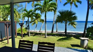 Un espacio de estar techado al aire libre con vista a la playa y palmeras.