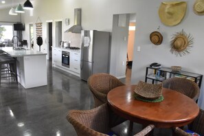 A modern kitchen with stainless steel appliances, a dining area with wicker chairs, and a variety of hats on the wall. - Moana Sunset Beach Villa (Rarorotnga)