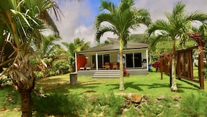 Una casa moderna con un porche cubierto, rodeada de abundante vegetación y palmeras.