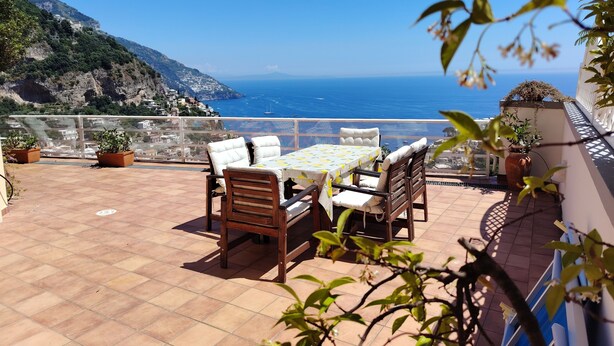 Une terrasse avec une table et des chaises, offrant une vue sur la côte et sur une montagne en arrière-plan.