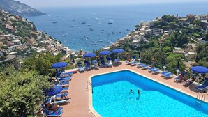 Une piscine dotée de chaises longues et de parasols, entourée de bâtiments et offrant une vue sur la mer.