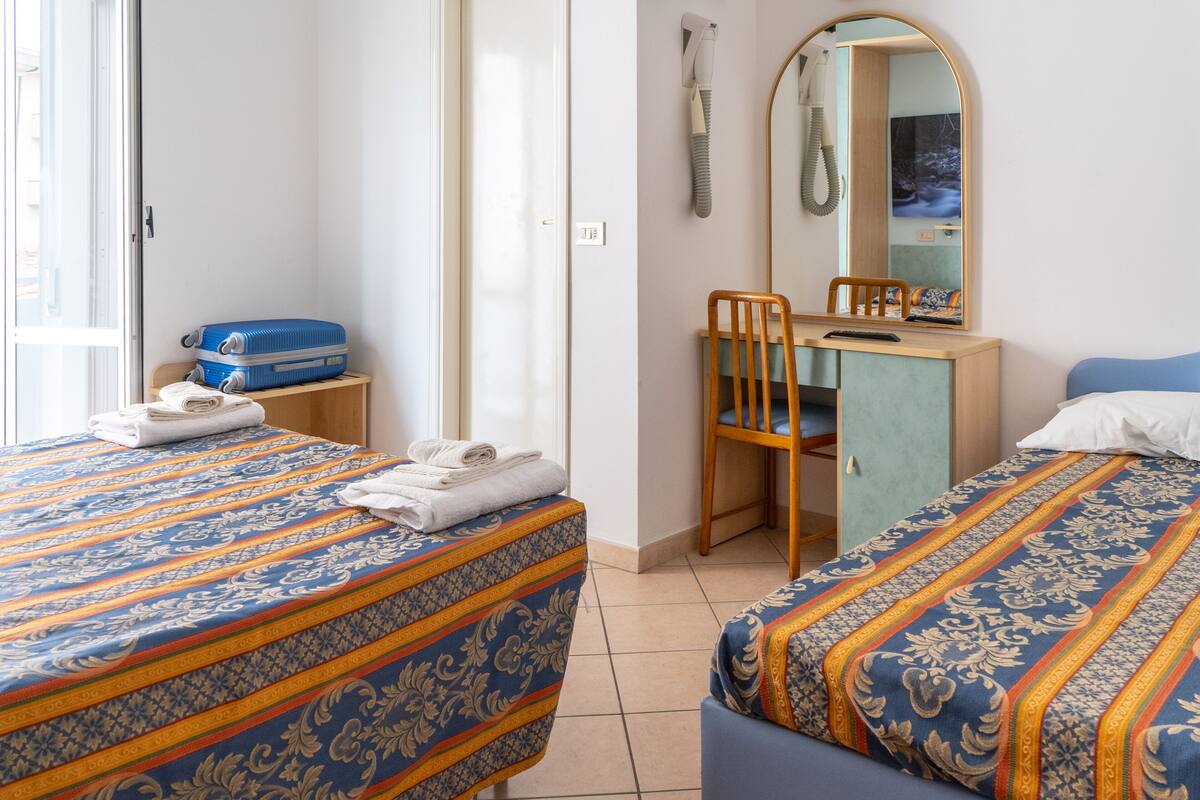 A hotel room with two beds, a desk, a chair, a suitcase, and a mirror.