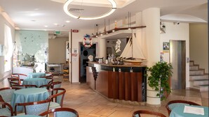 Un restaurant avec des tables et des chaises rondes, un bar décoré sur le thème d’un navire et un escalier menant à un étage supérieur.