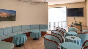 A lounge area with a curved sofa, multiple round tables, and chairs. - Hotel Tiglio (Rimini)