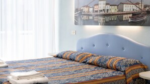 A hotel room with two beds, each with a patterned blue and orange bedspread, and a neatly folded white towel on each bed. - Hotel Tiglio (Rimini)