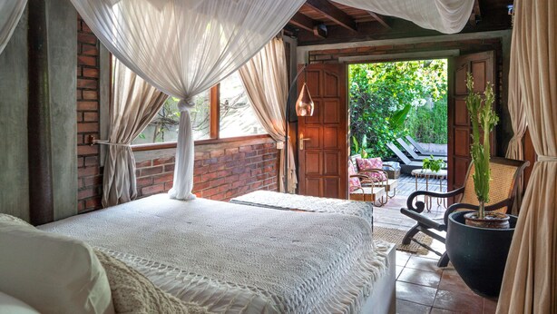 Un dormitorio con cama a dosel, vistas al jardín y una puerta de madera que da al exterior.
