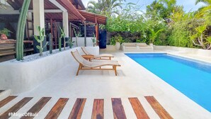 Un área de piscina con sillas de descanso, un muelle de madera y un jardín de cactus.