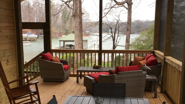 A covered outdoor seating area with a table and chairs, a rocking chair, and a view of a lake and dock.