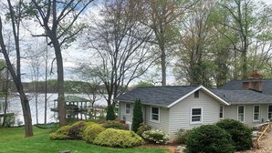 A single-story house with a sloped roof, surrounded by a well-maintained lawn and a dock extending into a calm lake.