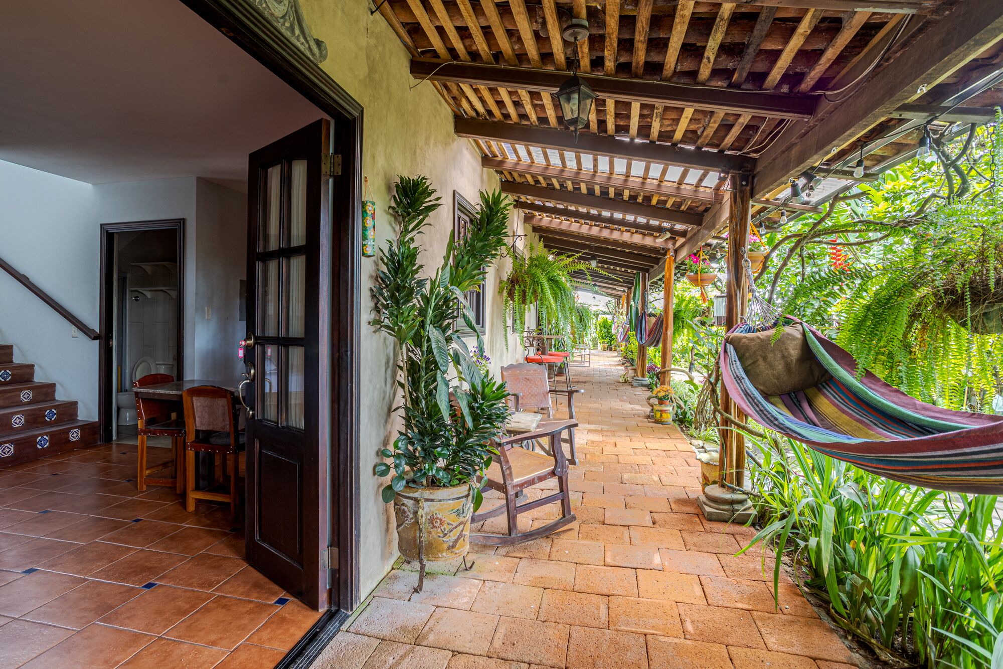 A covered outdoor area with a hammock, potted plants, and a wooden table.