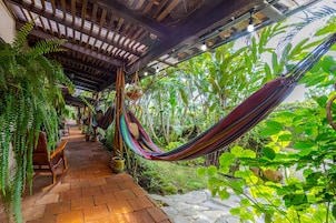A covered outdoor area with a hammock, wooden benches, and lush greenery.