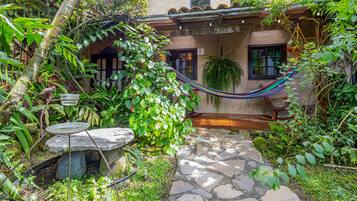 A stone pathway leading to a rustic building with a hammock and a stone bench.