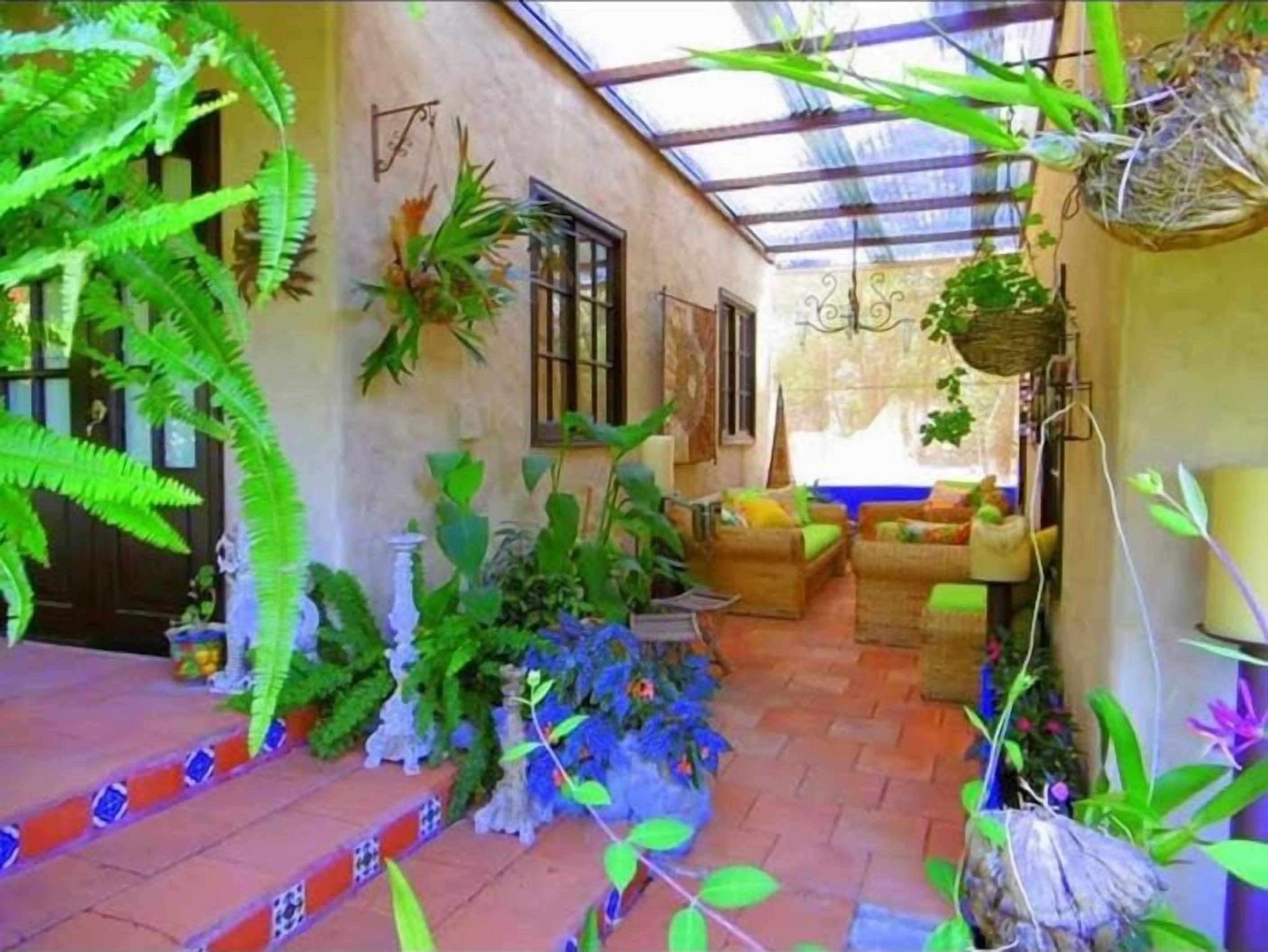 A covered patio area with wicker furniture, potted plants, and a stone floor.