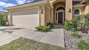 A single-story house with a beige facade, a garage, and a well-maintained front yard with various plants. - South Padre Paradise w/ Saltwater Pool Near Golf! (Laguna Vista)