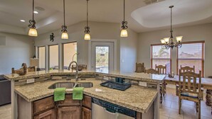 A kitchen with granite countertops, a dishwasher, a sink, and a dining area with wooden chairs. - South Padre Paradise w/ Saltwater Pool Near Golf! (Laguna Vista)