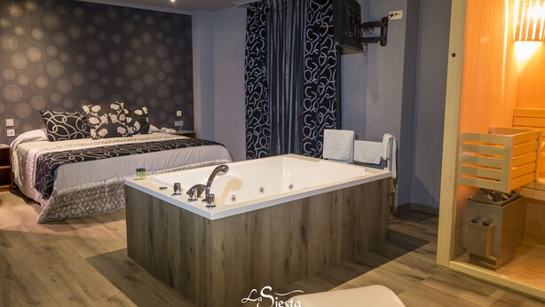 Una habitación de hotel moderna con una bañera grande, una cama con ropa de cama estampada y piso de madera.