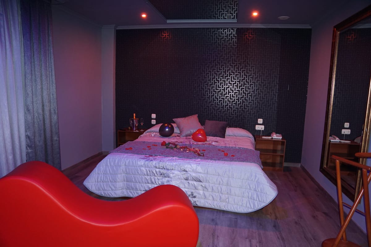 A bedroom with a bed, red chairs, and a patterned wall.