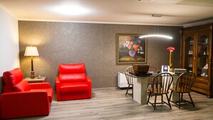 Una sala de estar con un sofá rojo, un sillón rojo, una mesa de comedor con sillas, una lámpara y un cuadro en la pared.