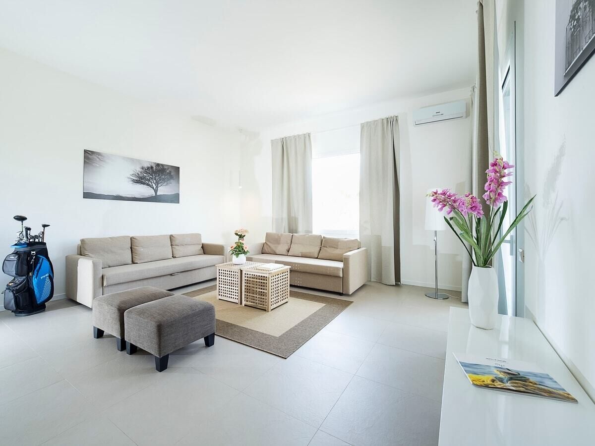 A modern living room with a sofa set, ottoman, and a coffee table. There is a golf bag and a vase with flowers on a side table.