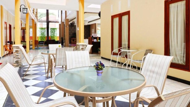 Eine Hotellobby mit Schachbrettfußboden, runden Tischen mit Stühlen und einem Glastisch mit Blumenarrangement.