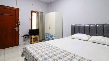Un dormitorio con cama, armario, televisor sobre una mesa de madera y una puerta.