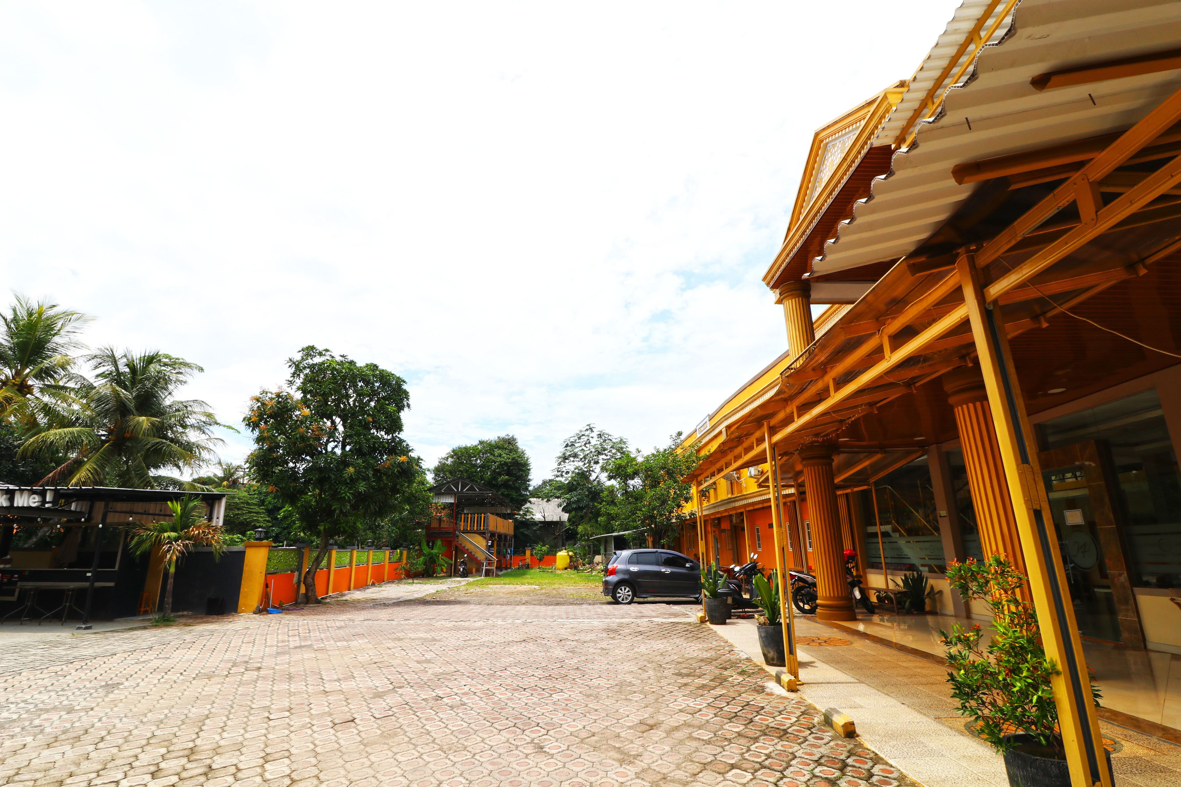 A hotel entrance with a paved driveway, a parked car, and a motorcycle.