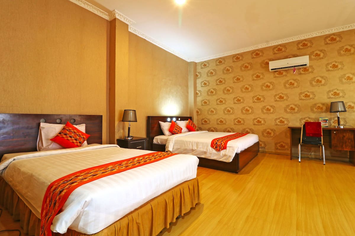 A hotel room with two beds, a desk, a chair, and an air conditioning unit on the wall.