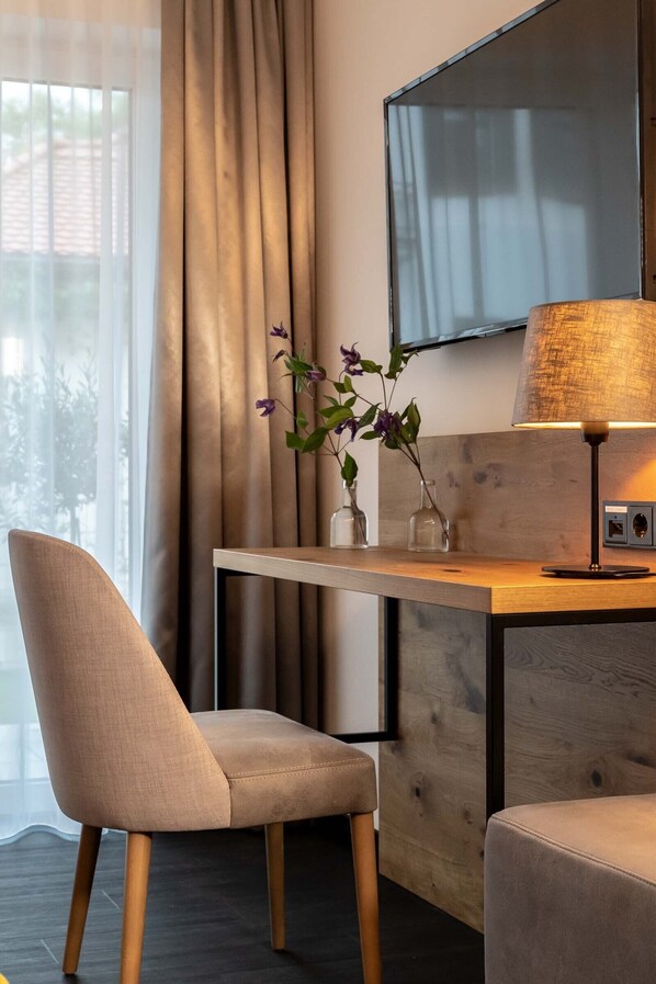 Una habitación moderna con un escritorio de madera, una silla, un sofá, un televisor montado en la pared y una lámpara.