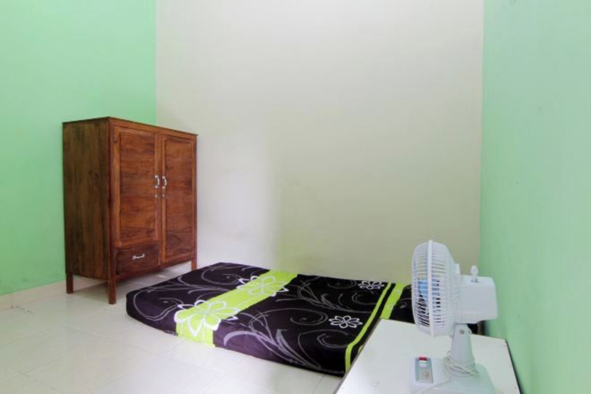 A small room with a wooden cabinet, a bed with a floral bedspread, and a white fan.