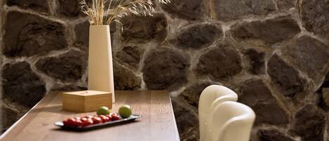 A stone wall, a wooden table with a vase, a wooden box, and a plate with fruit.